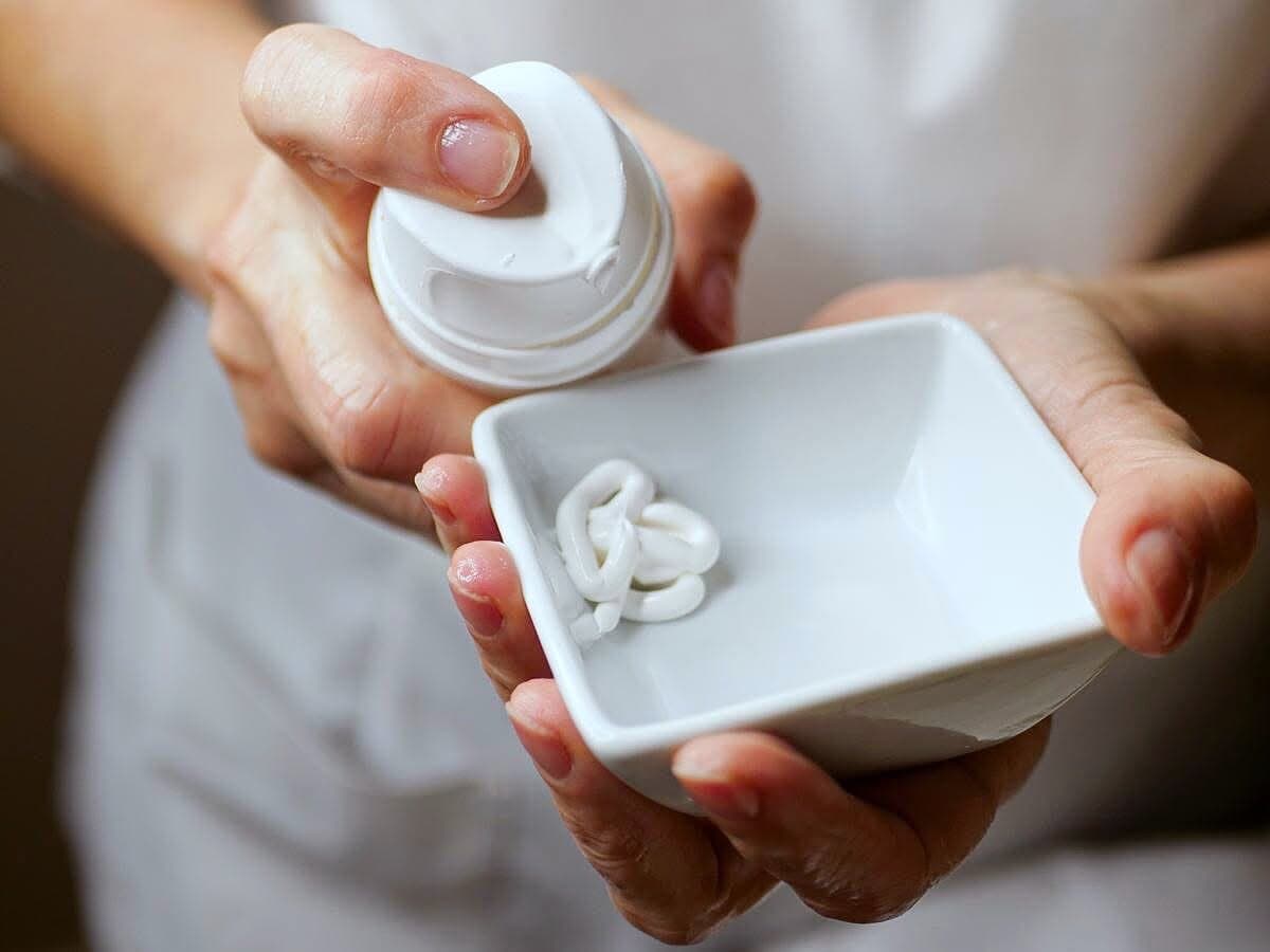 Le mani versano una crema bianca in una ciotolina di porcellana